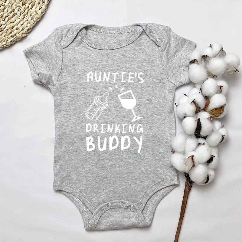 Grey baby onesie with 'Auntie's Drinking Buddy' text on a white background with cotton and woven mat.