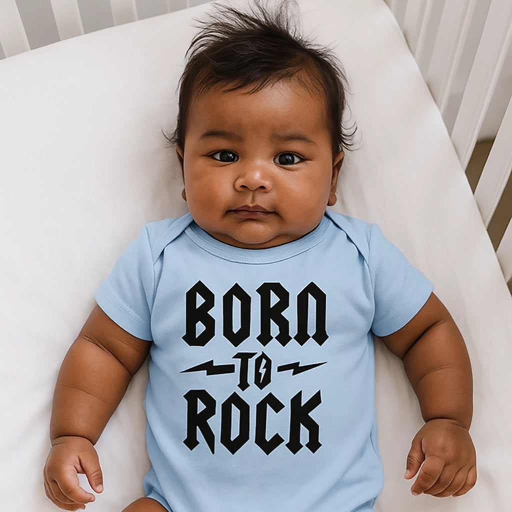 Baby wearing a light blue onesie with 'Born to Rock' text, lying on a white surface.