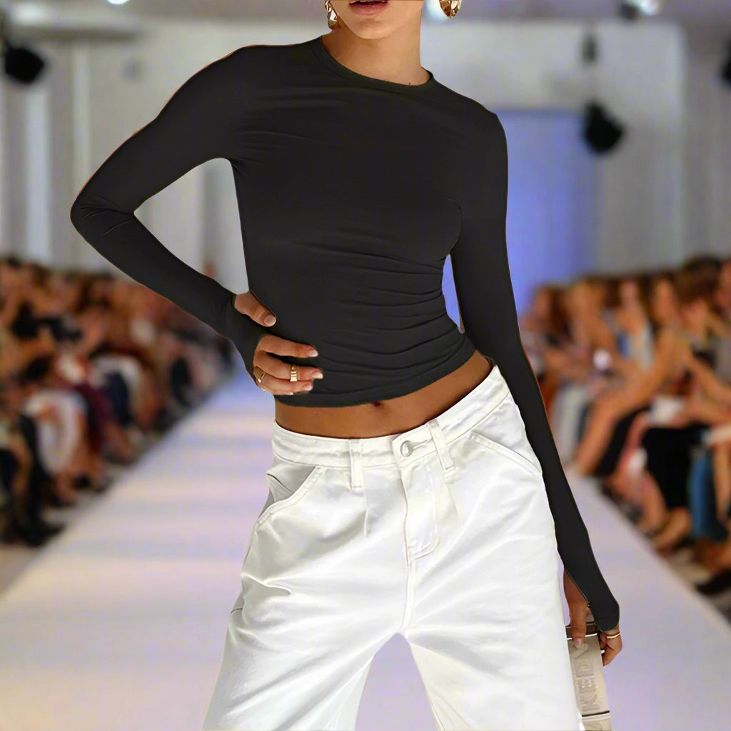 Model wearing a black long-sleeve top and white pants on a fashion runway.