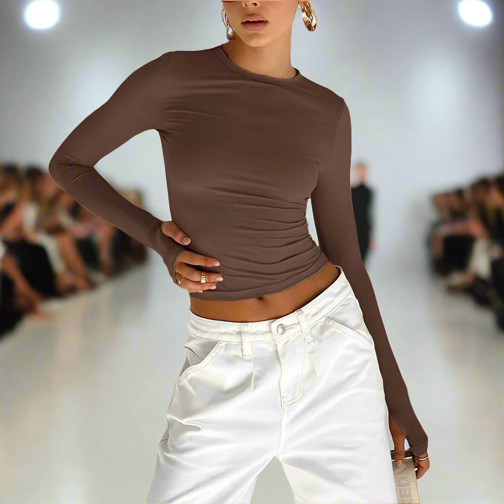 Model on a fashion runway wearing a brown long-sleeve top and white pants.