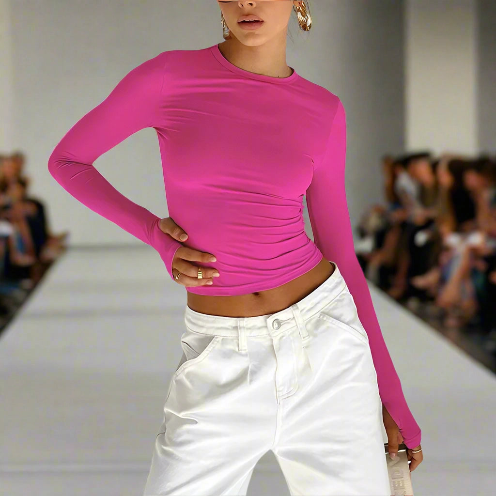 Model wearing a bright pink long-sleeve top and white pants on a runway.