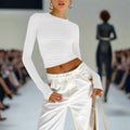 Model wearing a white long-sleeve top and pants on a fashion runway.
